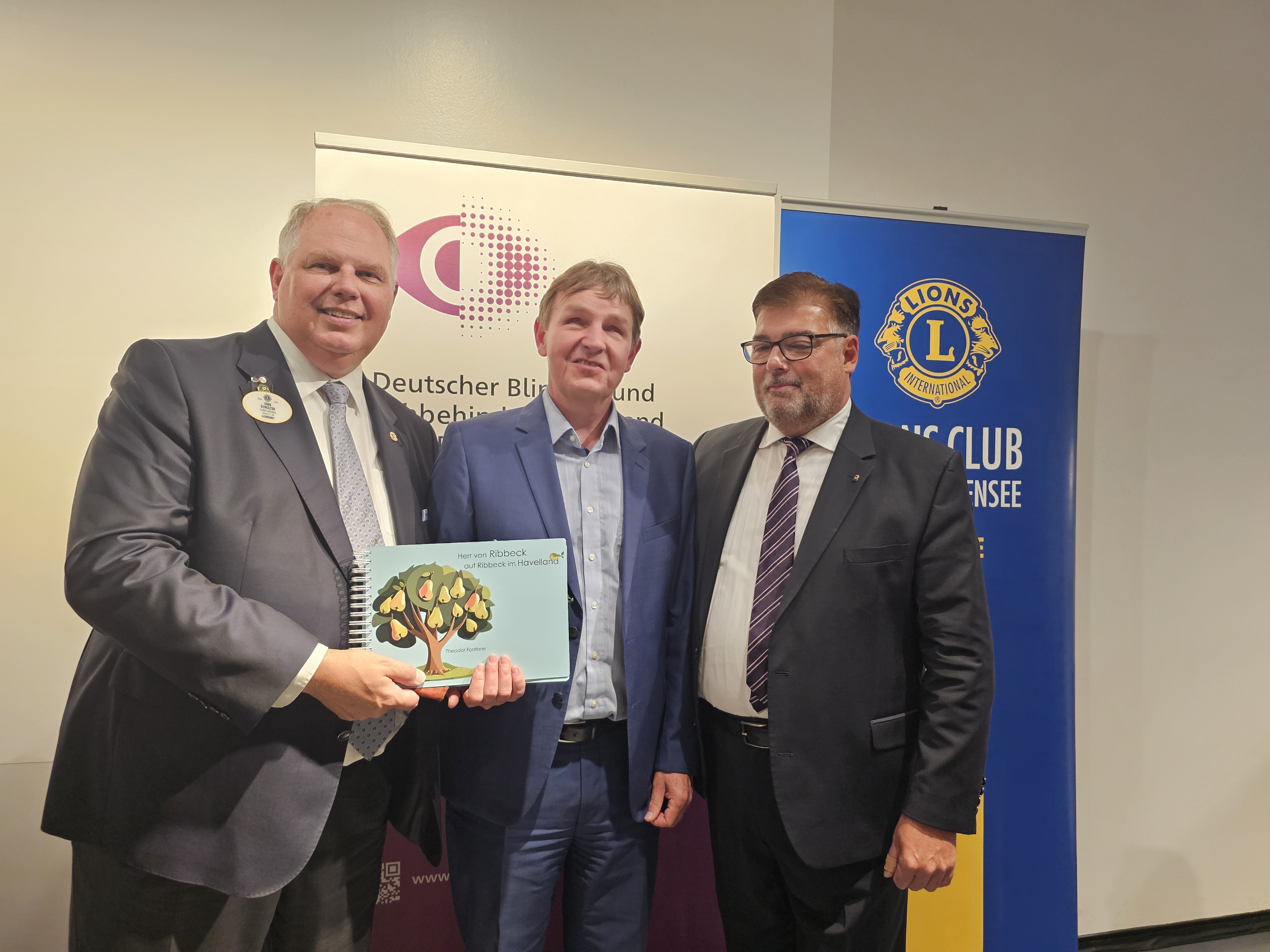 DBSV-Geschäftsführer Andreas Bethke (Mitte) übergibt ein Exemplar des Tastbuches "Herr von Ribbeck auf Ribbeck im Havelland" an Lions Distrikt-Governor Uwe Schulteß (links) und DBS-Vorstand Thomas Waterstradt (rechts).
