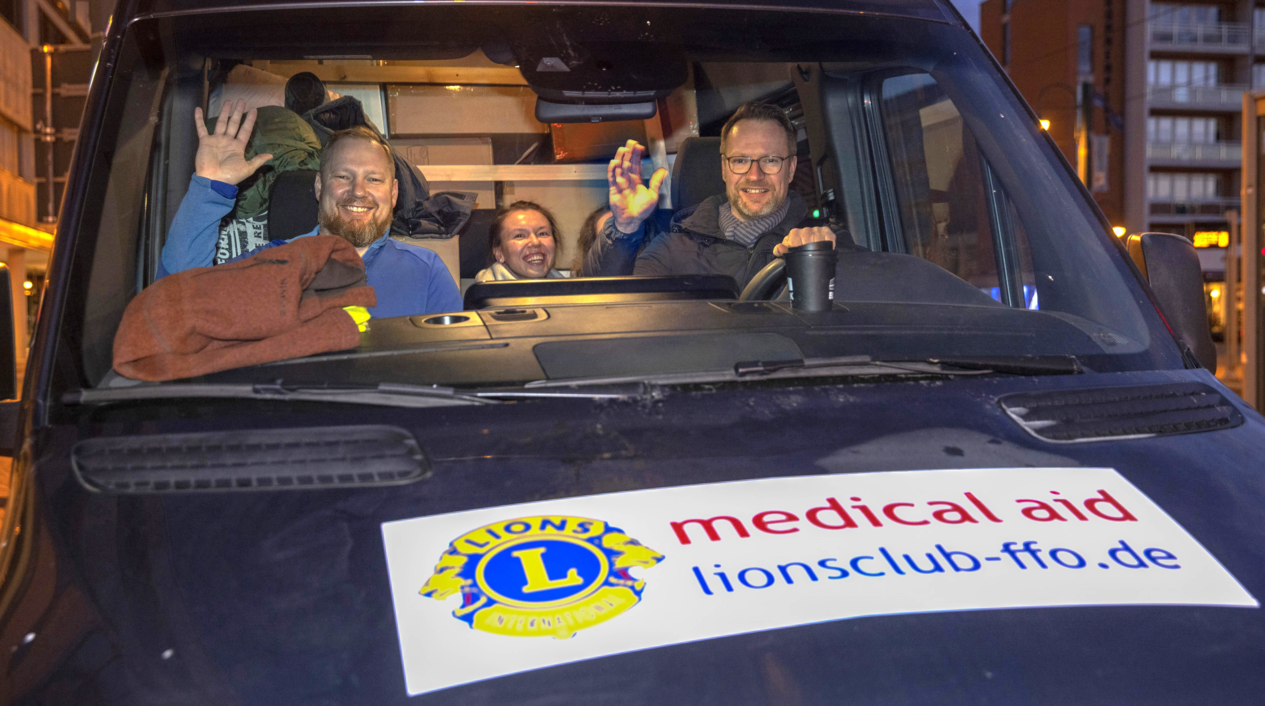 Drei Personen sitzen in einem Auto und winken